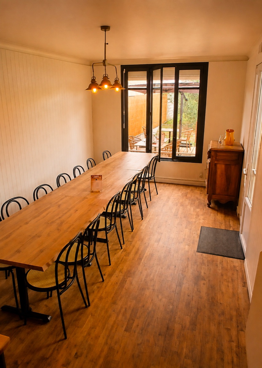 La petite salle à l'arrière : longue table en bois, chaises bistrot et porte-fenêtre ouvrant sur la terrasse